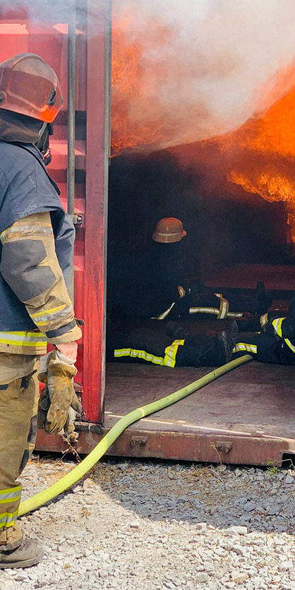 Brandschutzhelfer bei der Übrung, Flammen und Rauch in einem dunklen Container