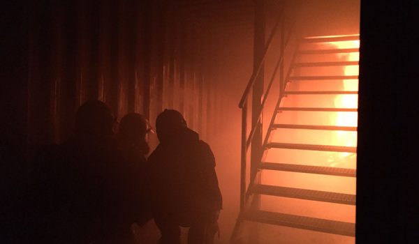 Brandschutzhelfer bei der Übrung, Flammen und Rauch in einem dunklen Raum mit Treppe