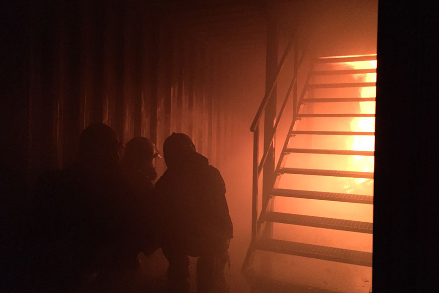 Brandschutzhelfer bei der Übrung, Flammen und Rauch in einem dunklen Raum mit Treppe