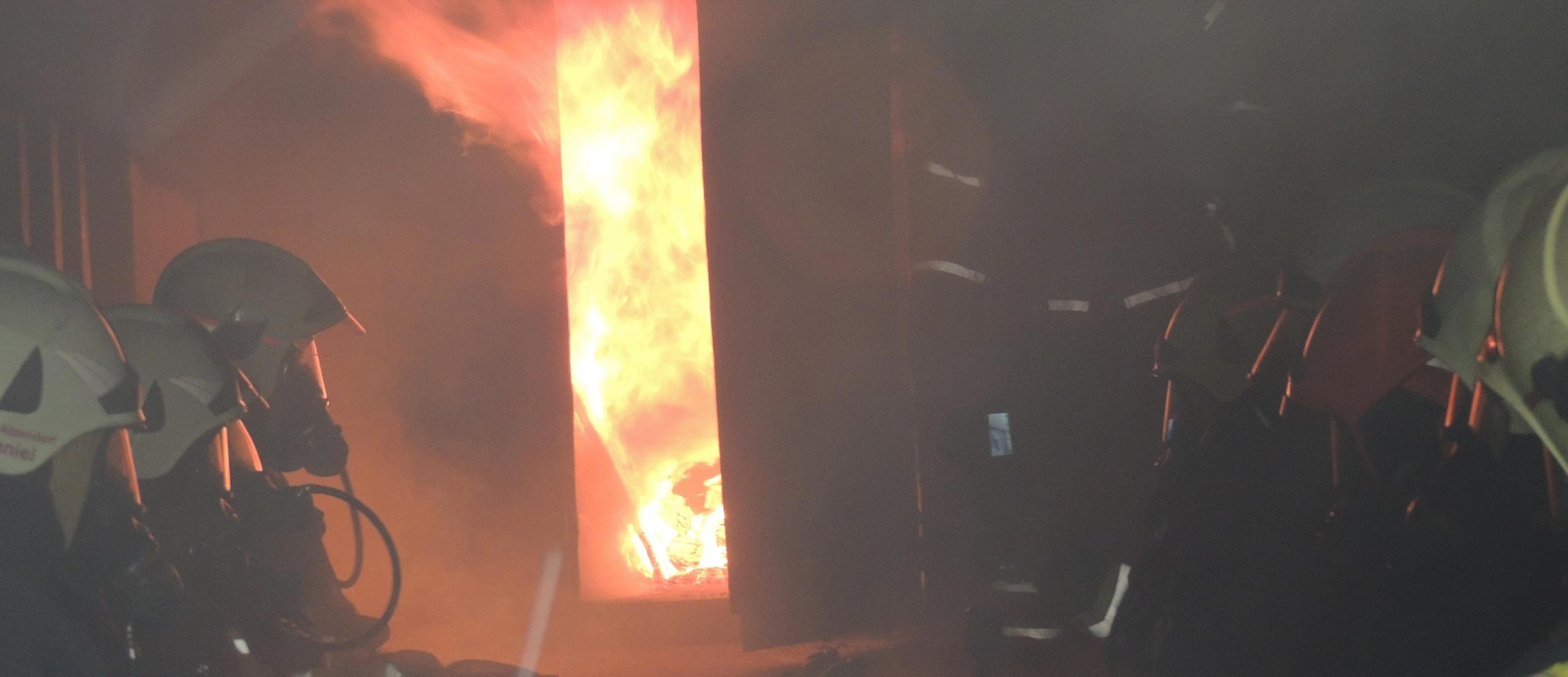 Flammen schlagen durch eine offene Tür eines Übungscontainers